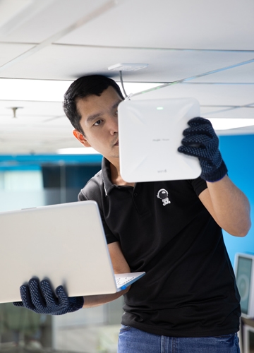 IT technician configuring a white wireless access point while holding a laptop