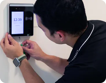 An IT support professional installs a biometric access management device on a office wall